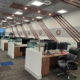 Open office workstations with white end panels and wood-grain desks under a diagonal wood slat ceiling at TBX Freight
